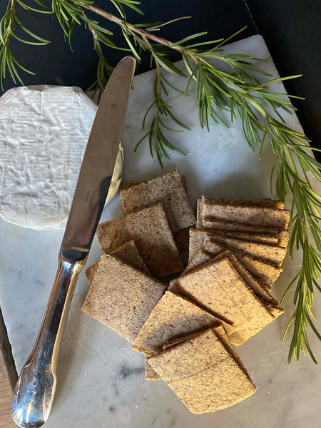 Galleta de harina de almendras, chia, aceite de oliva. decorado con una rama de romero, queso y un cuchillo